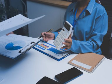 Ofiste çalışan denetçi ve muhasebeci ekibi mali verileri ve muhasebe kayıtlarını hesap makinesiyle analiz ediyor. Muhasebe şirketi kârlı nakit akışı için finansman ve vergilendirme planlaması sağlıyor.