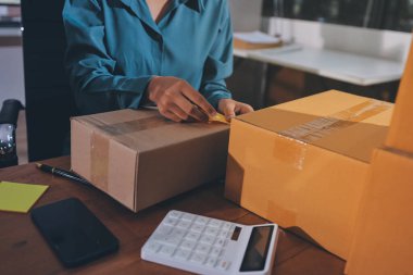 Girişim KOBİ küçük işletme girişimcisi önlük giyen Asyalı kadın dizüstü bilgisayar ve kutu kullanarak çevrimiçi müşterilere, çevrimiçi sme iş fikirlerine satış hazırlamak için siparişleri alır ve gözden geçirir.