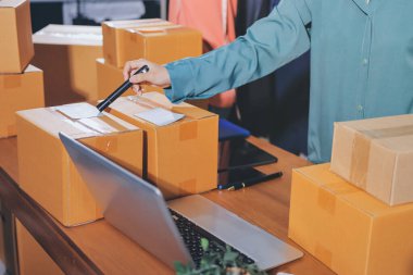 Girişim KOBİ küçük işletme girişimcisi önlük giyen Asyalı kadın dizüstü bilgisayar ve kutu kullanarak çevrimiçi müşterilere, çevrimiçi sme iş fikirlerine satış hazırlamak için siparişleri alır ve gözden geçirir.