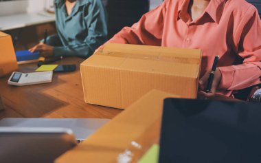 Girişim KOBİ küçük işletme girişimcisi önlük giyen Asyalı kadın dizüstü bilgisayar ve kutu kullanarak çevrimiçi müşterilere, çevrimiçi sme iş fikirlerine satış hazırlamak için siparişleri alır ve gözden geçirir.