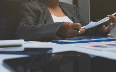 Ofiste çalışan denetçi ve muhasebeci ekibi mali verileri ve muhasebe kayıtlarını hesap makinesiyle analiz ediyor. Muhasebe şirketi kârlı nakit akışı için finansman ve vergilendirme planlaması sağlıyor.