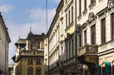 Klasik mimari ön cepheleri Krakow 'un tarihi merkezinde bir cadde, süslü neoklasik binalar ve arka planda yeşil bakır çatılı ayırt edici sarı bir bina. Polonya.