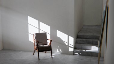 Boş bir sanat stüdyosunun ya da tefekkür odasının minimalist üç boyutlu iç mekanı. Ahşap ve kumaş sandalye güçlü bir öğleden sonra güneşi ve gölgeyle yıkandı. Şövalesi ve merdivenleri olan modern, boş bir oda. Barış, yalnızlık, sanat ve tasarım kavramı.