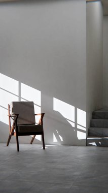 Boş bir sanat stüdyosunun ya da tefekkür odasının minimalist üç boyutlu iç mekanı. Ahşap ve kumaş sandalye güçlü bir öğleden sonra güneşi ve gölgeyle yıkandı. Şövalesi ve merdivenleri olan modern, boş bir oda. Barış, yalnızlık, sanat ve tasarım kavramı.