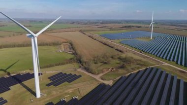 Büyük rüzgar türbini ve güneş paneli dizisinin hava aracı görüntüsü, yenilenebilir enerji santrali güneşli bahar sabahı Birleşik Krallık. Elektrik gücü..
