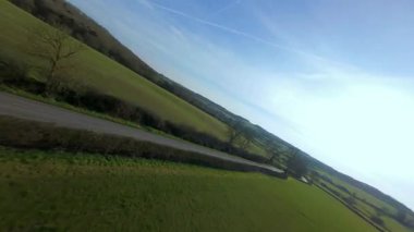 FPV insansız hava aracı gün batımında İngiltere 'nin yeşil arazilerinden geçer, çiftlik hayvanlarının, çitlerin ve çayırların yanından geçer, yukarıdan kırsal manzaranın güzelliğini yakalar.