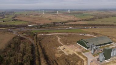 Arka planda rüzgar türbinleri, kırsal arazi ve sürdürülebilir kaynaklar, Kettering, Birleşik Krallık 'ta bulunan büyük tarım ambarlarının ve siloların havadan görünüşü