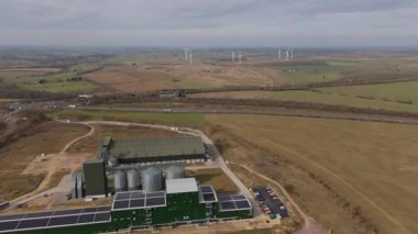 Arka planda rüzgar türbinleri, kırsal arazi ve sürdürülebilir kaynaklar, Kettering, Birleşik Krallık 'ta bulunan büyük tarım ambarlarının ve siloların havadan görünüşü