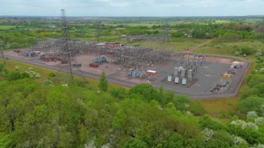 Elektrik hatları pilonları ve transformatörlerle elektrik şebekesine güç aktaran hava aracı görüntüsü.