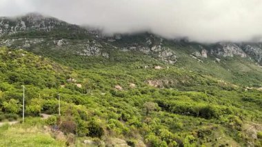 Karadağ 'ın Kotor kentindeki dev dağ sıralarının havadan görünüşü, yemyeşil bir manzara, baharda bulutlu bir zirve. Yollar rüzgarlı yılan şeritleri. Avrupa Seyahati.