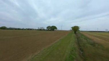 FPV insansız hava aracı görüntüsü, İngiltere 'deki rüzgar türbinleri ve kırsal alanlar üzerinden alçak geçiş yapıyor.