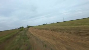 FPV insansız hava aracı görüntüsü, İngiltere 'deki rüzgar türbinleri ve kırsal alanlar üzerinden alçak geçiş yapıyor.