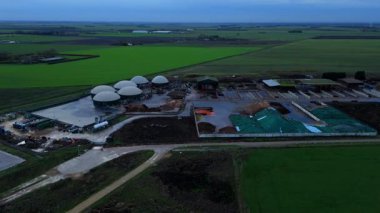 Modern bir yenilenebilir enerji biyogaz santralinin insansız hava aracı görüntüsü tarım atıklarını İngiltere kırsalında yeşil elektriğe dönüştürüyor..