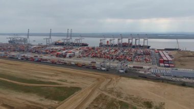Bir sürü yük konteynırı ve büyük kargo gemisi kenetlenmiş büyük bir nakliye limanının insansız hava aracı görüntüsü, Gri trenler ve ithalat için malları taşıyan HGV 'ler, Londra Thames UK kapısı.