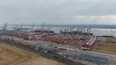 Bir sürü yük konteynırı ve büyük kargo gemisi kenetlenmiş büyük bir nakliye limanının insansız hava aracı görüntüsü, Gri trenler ve ithalat için malları taşıyan HGV 'ler, Londra Thames UK kapısı.