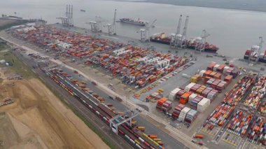 Bir sürü yük konteynırı ve büyük kargo gemisi kenetlenmiş büyük bir nakliye limanının insansız hava aracı görüntüsü, Gri trenler ve ithalat için malları taşıyan HGV 'ler, Londra Thames UK kapısı.