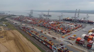 Bir sürü yük konteynırı ve büyük kargo gemisi kenetlenmiş büyük bir nakliye limanının insansız hava aracı görüntüsü, Gri trenler ve ithalat için malları taşıyan HGV 'ler, Londra Thames UK kapısı.