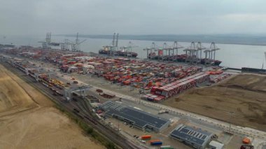 Bir sürü yük konteynırı ve büyük kargo gemisi kenetlenmiş büyük bir nakliye limanının insansız hava aracı görüntüsü, Gri trenler ve ithalat için malları taşıyan HGV 'ler, Londra Thames UK kapısı.