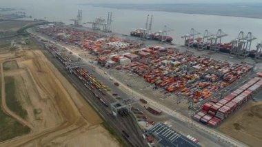 Bir sürü yük konteynırı ve büyük kargo gemisi kenetlenmiş büyük bir nakliye limanının insansız hava aracı görüntüsü, Gri trenler ve ithalat için malları taşıyan HGV 'ler, Londra Thames UK kapısı.