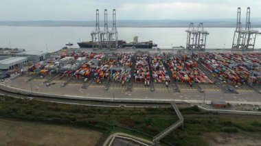 Bir sürü yük konteynırı ve büyük kargo gemisi kenetlenmiş büyük bir nakliye limanının insansız hava aracı görüntüsü, Gri trenler ve ithalat için malları taşıyan HGV 'ler, Londra Thames UK kapısı.