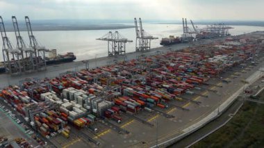 Bir sürü yük konteynırı ve büyük kargo gemisi kenetlenmiş büyük bir nakliye limanının insansız hava aracı görüntüsü, Gri trenler ve ithalat için malları taşıyan HGV 'ler, Londra Thames UK kapısı.
