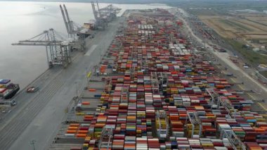 Bir sürü yük konteynırı ve büyük kargo gemisi kenetlenmiş büyük bir nakliye limanının insansız hava aracı görüntüsü, Gri trenler ve ithalat için malları taşıyan HGV 'ler, Londra Thames UK kapısı.