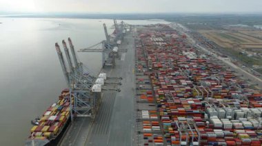 Bir sürü yük konteynırı ve büyük kargo gemisi kenetlenmiş büyük bir nakliye limanının insansız hava aracı görüntüsü, Gri trenler ve ithalat için malları taşıyan HGV 'ler, Londra Thames UK kapısı.