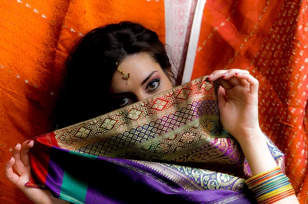 The young dark-haired woman hides a face behind a piece of colorful Indian saris. Indian style. — Stock Photo, Image