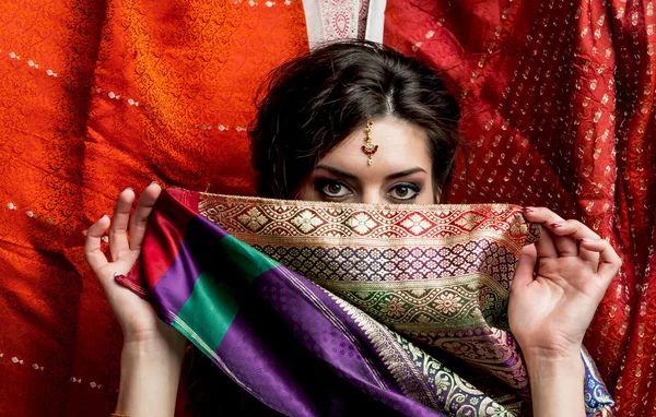 Mladá černovlasá žena skrývá tvář za kus barevné indické sárí. Indický styl. — Stock fotografie