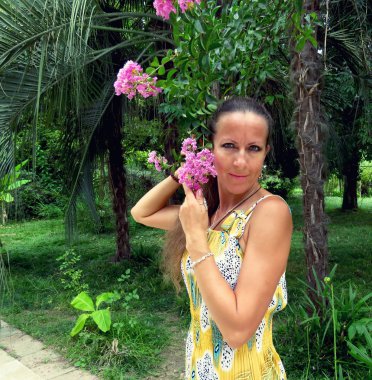 Tropikal bir park arka plan ağaç çiçek açması bir dalı yüz için bir renkli yaz içinde genç bir kadın presler