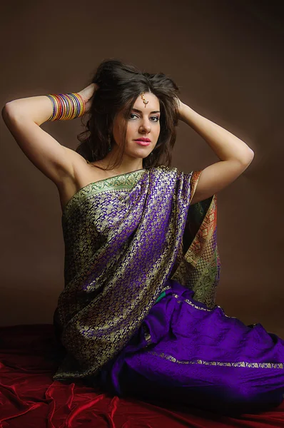 Mujer joven en los ricos saris indios y pulseras de colores sentado con las manos con volantes pelo. Estilo indio . — Foto de Stock