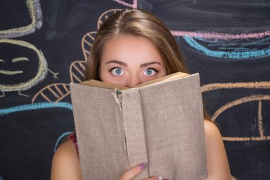 Genç öğrenci kız bir kitap saklanıyor korkmuş gözleri