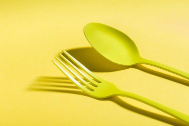 Sarı çatal bıçak seti sarı arka plana gölge düşürüyor.