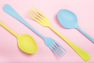 Kaşıklar ve çatallar pembe arka planda sarı ve mavi