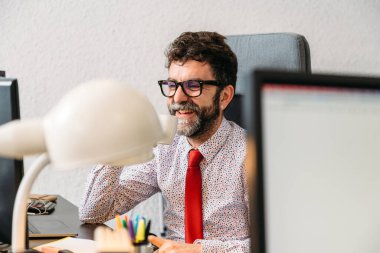 Gülümseyen orta yaşlı, sakallı ve gözlüklü bir yönetici. Video konferansı sırasında kahve içiyor.