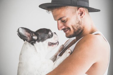 Kollarında beyaz arka planda Fransız Bulldog köpeği olan piercingli dövmeli çocuk.