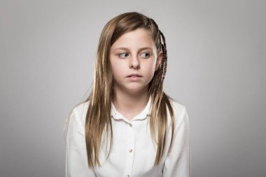 Studio portrait of a cute girl with long blonde hair looking askance against neutral background