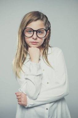 Studio portrait of a cute girl with long blonde hair wearing glasses against neutral background