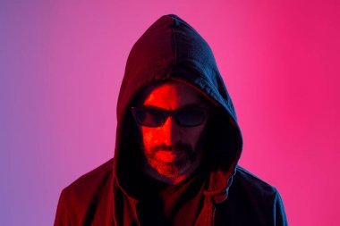 Colorful studio portrait of a bearded man with sunglasses against red and blue background.
