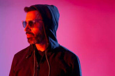 Colorful studio portrait of a bearded man with sunglasses against red and blue background.