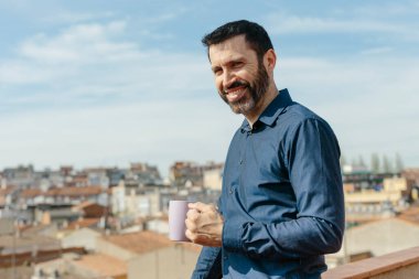 Relaxing moment of a middle-aged man standing on the balcony drinking coffee