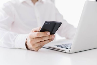 Close-up view of professional businessman using smartphone against white desk