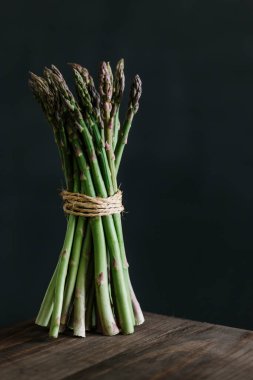 Bunch of raw fresh asparagus on wooden table against black background.