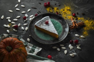 Güzel bir parça balkabağı turtası yaban mersinli ve taş bir masanın üzerinde pudra şekerli. Yakınlarda balkabağı ve tarçın çubukları var. Üst görünüm