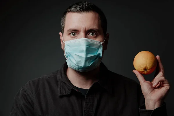 white young man in a medical mask, European, on a dark background, with a tangerine