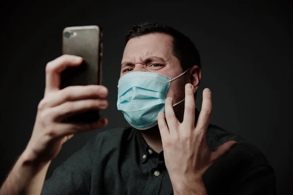 Avrupalı beyaz bir adam, tıbbi maske takıyor, kızgın, cep telefonuna bağırıyor. Ambulans çalışmıyor, arama sorunu var. Üzgün ve öfkeli..