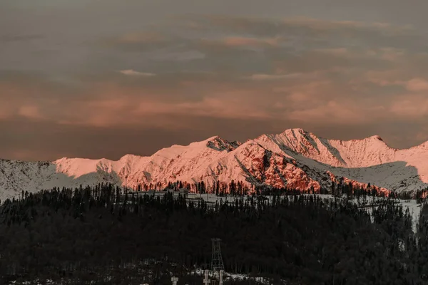Adler, Rosa Khutor. Akşam dağlarının göz kamaştırıcı manzarası. Dağların tepelerinde kar var, güneş yavaşça batıyor, gün batımı....