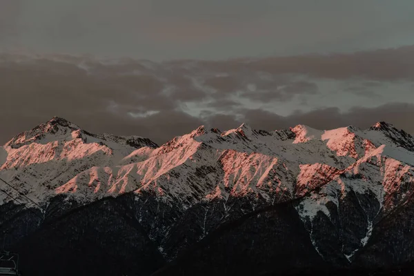 Adler, Rosa Khutor. Akşam dağlarının göz kamaştırıcı manzarası. Dağların tepelerinde kar var, güneş yavaşça batıyor, gün batımı....