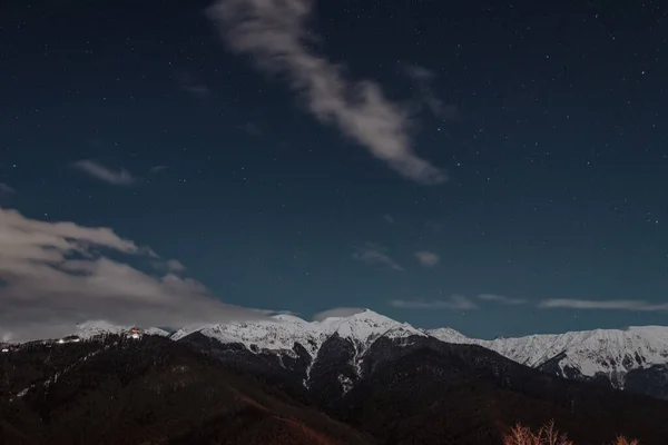 Adler, Rosa Khutor. Geceleri dağların uzun pozlu fotoğrafı. Gökyüzünde bir sürü yıldız var, dağların tepesinde kar yatıyor. Kış