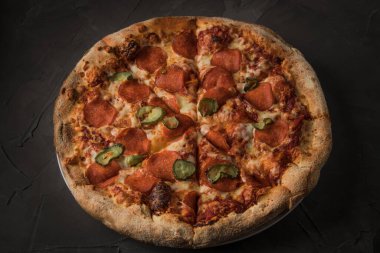 Karanlık taş bir masada salamlı ve salatalıklı lezzetli pizza. Üst görünüm